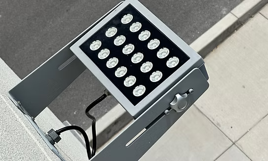 A gray metal LED bollard light fixture with 24 white circular LED chips on a black faceplate, mounted on a light gray stone pillar outdoors.