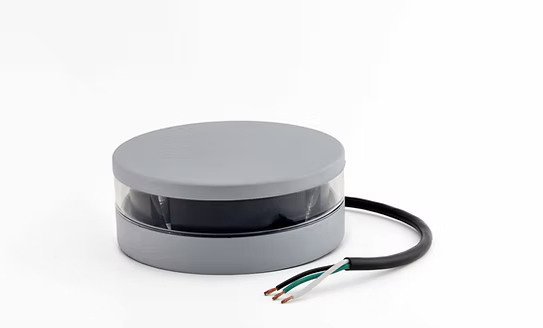 A gray circular electronic sensor or device with a clear window showing internal components, featuring a black cable with three exposed wires on a white background.