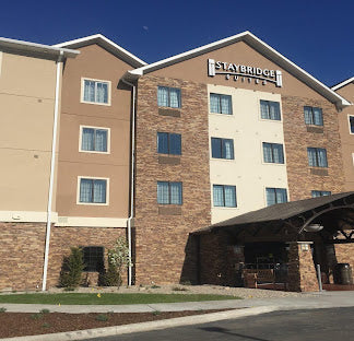 A multi-story Slayer Ridge Courtyard hotel building with beige and brown exterior walls, many windows, a covered entrance, and a clear blue sky above.