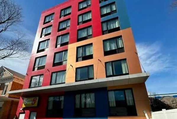 A tall modern building with a bold multicolor facade featuring large blocks of red, orange, blue, and teal, photographed against a clear blue sky.