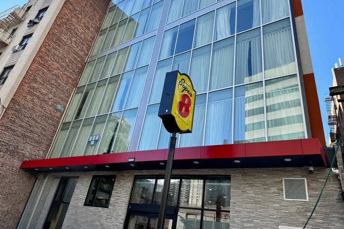 A 888 brand outdoor sign on a black pole in front of a modern glass and brick building, photographed from a low angle against a blue sky.